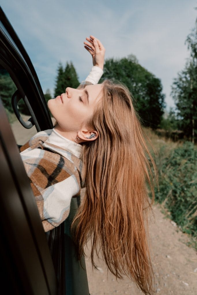 Kvinna lutar ut huvudet ur bilrutan bakåt, avslappnad och fri