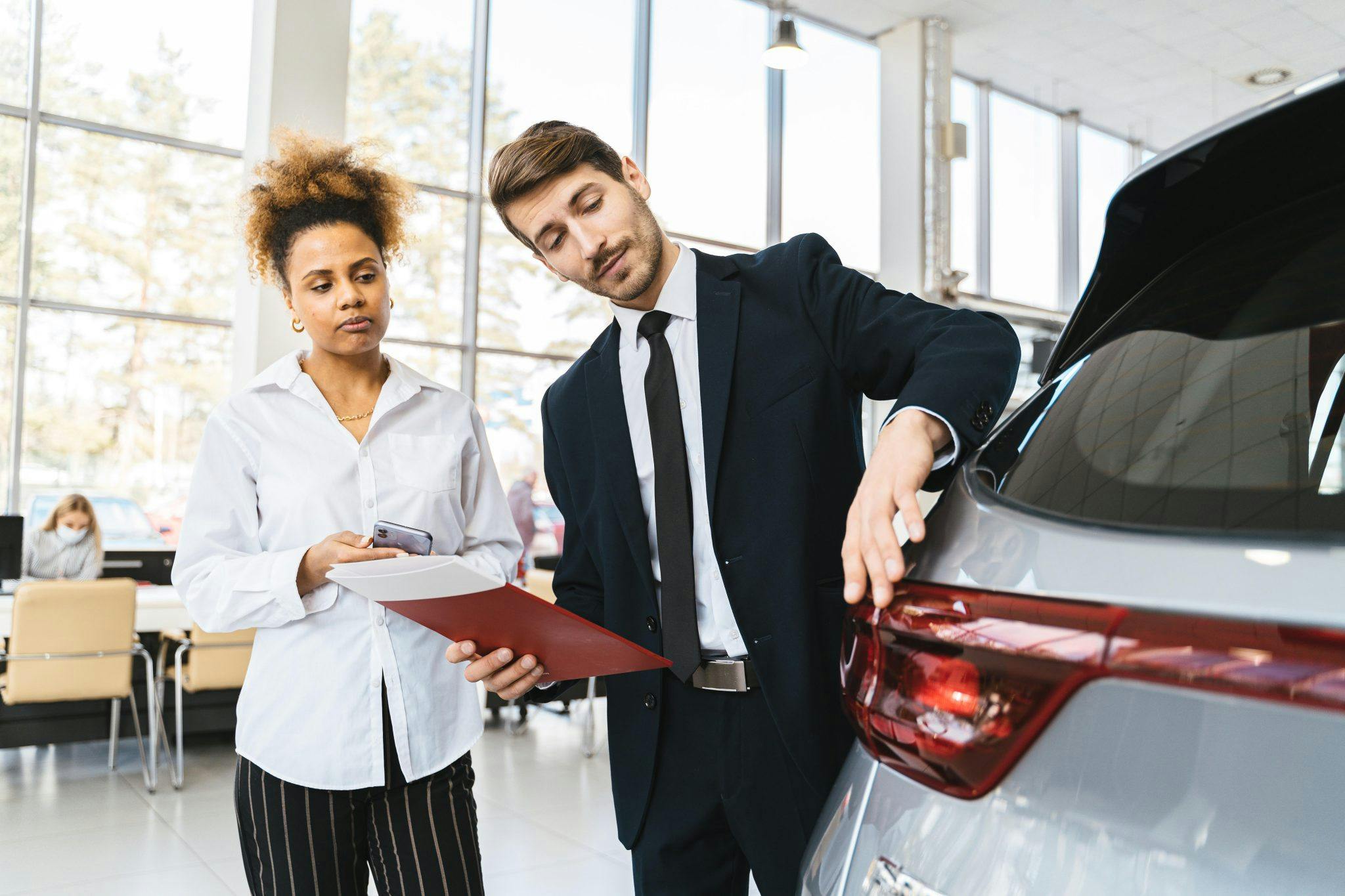 Manlig bilförsäljare i kostym talar med kvinnlig kund i en bilhall