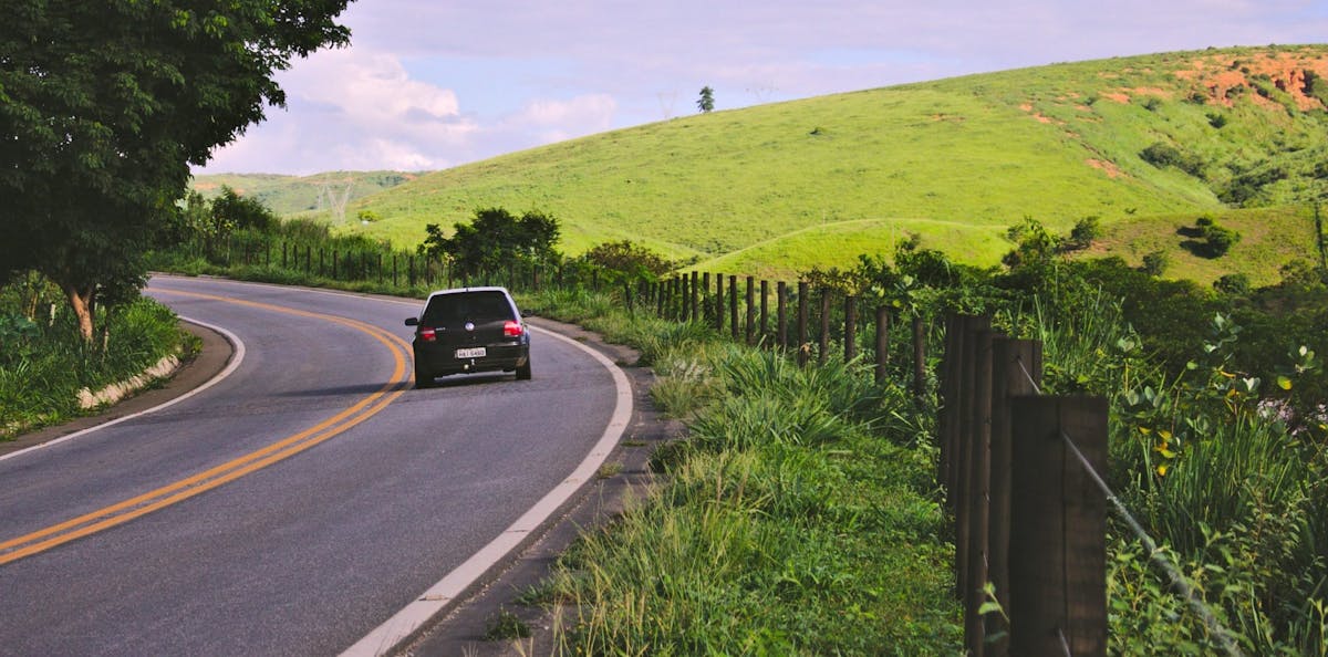 Bil kör på landsväg genom somrigt landskap med åker på högersidan
