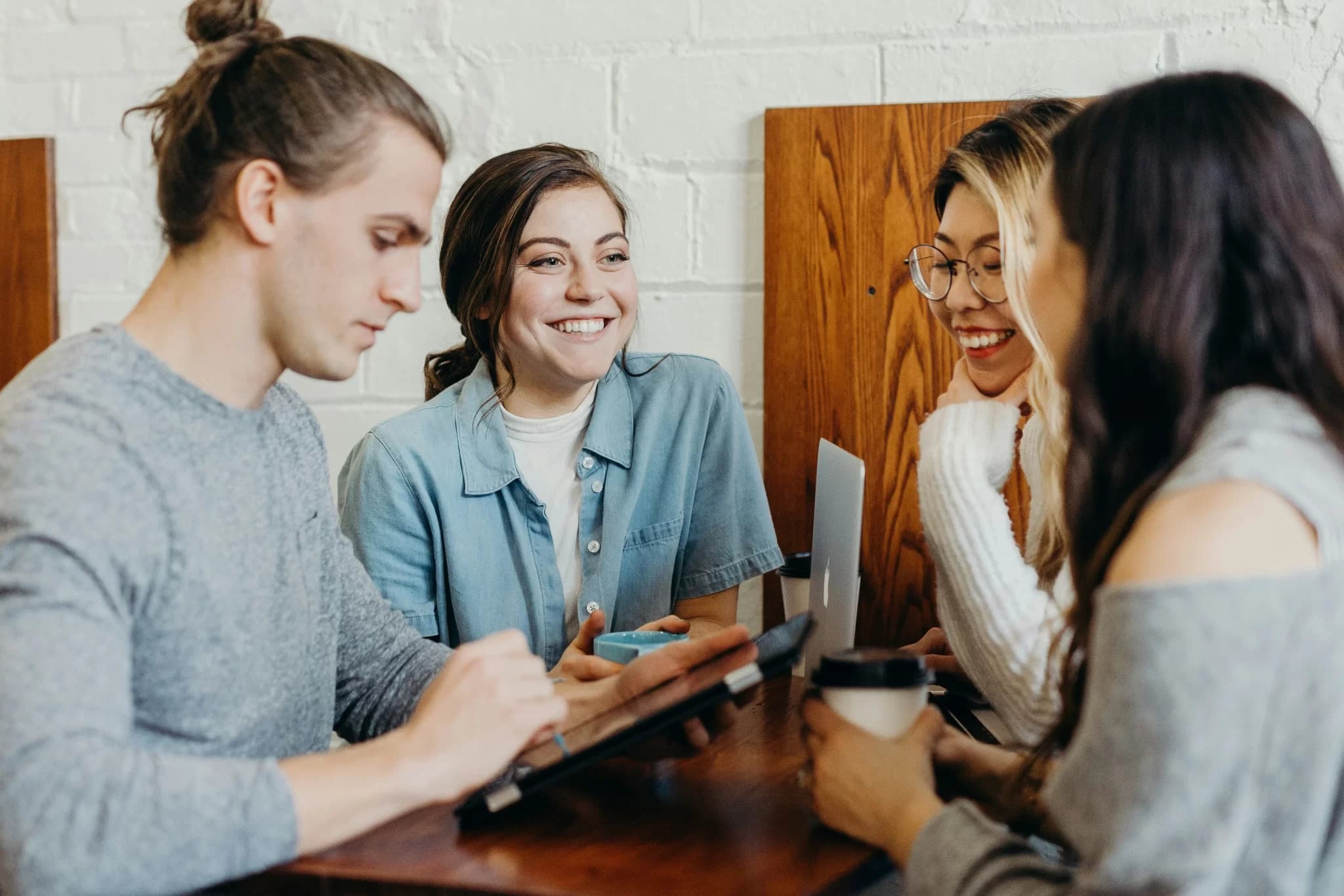 Grupp av tre kvinnor och en man sitter vid ett mötesbord, glada miner och kaffe